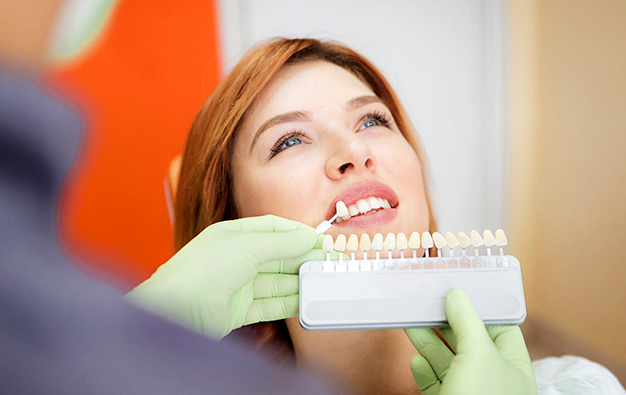Woman holding dental shade guide in dental office, smiling at dentist during consultation.