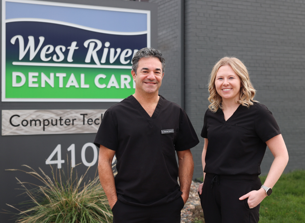 Two dental professionals in black scrubs stand outside West River Dental Care office building.