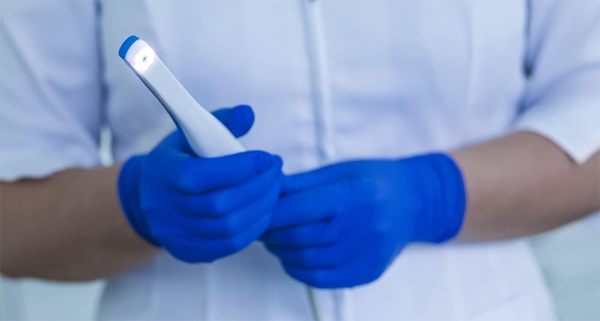Dentist in blue gloves holding dental mirror and suction tool in clinical setting.