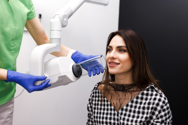 Dental professional in blue gloves examining smiling patient in checkered shirt at clinic.