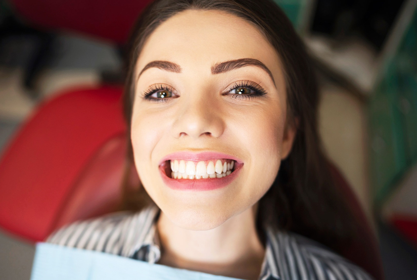 Smiling woman with dark hair in dental office setting, displaying bright healthy teeth.